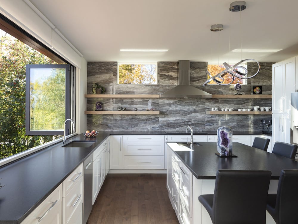 A kitchen remodel with a large window, black stone countertops, white cabinets, and an island with seating by Petra Custom Builders in Boulder County, CO A kitchen remodel with a large window, black stone countertops, white cabinets, and an island with seating by Petra Custom Builders in Boulder County, CO