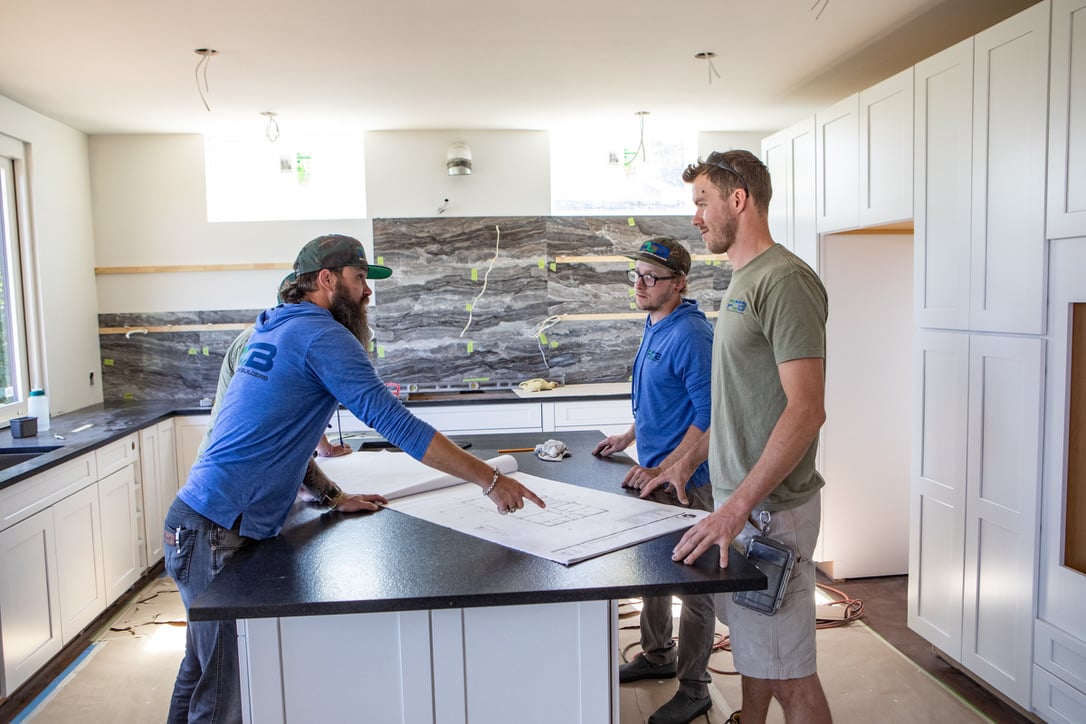 Petra Custom Builders team actively engaged in a kitchen construction discussion with blueprints on the island countertop