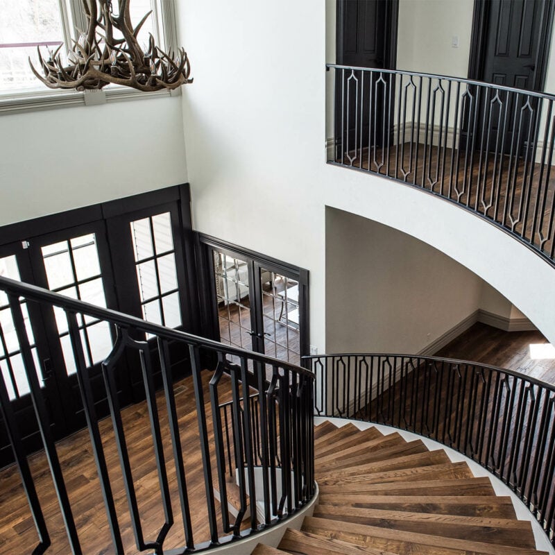 Elegant spiral staircase with dark wood steps, intricate iron railings, and a grand chandelier, highlighting the luxurious interior design by Petra Custom Builders