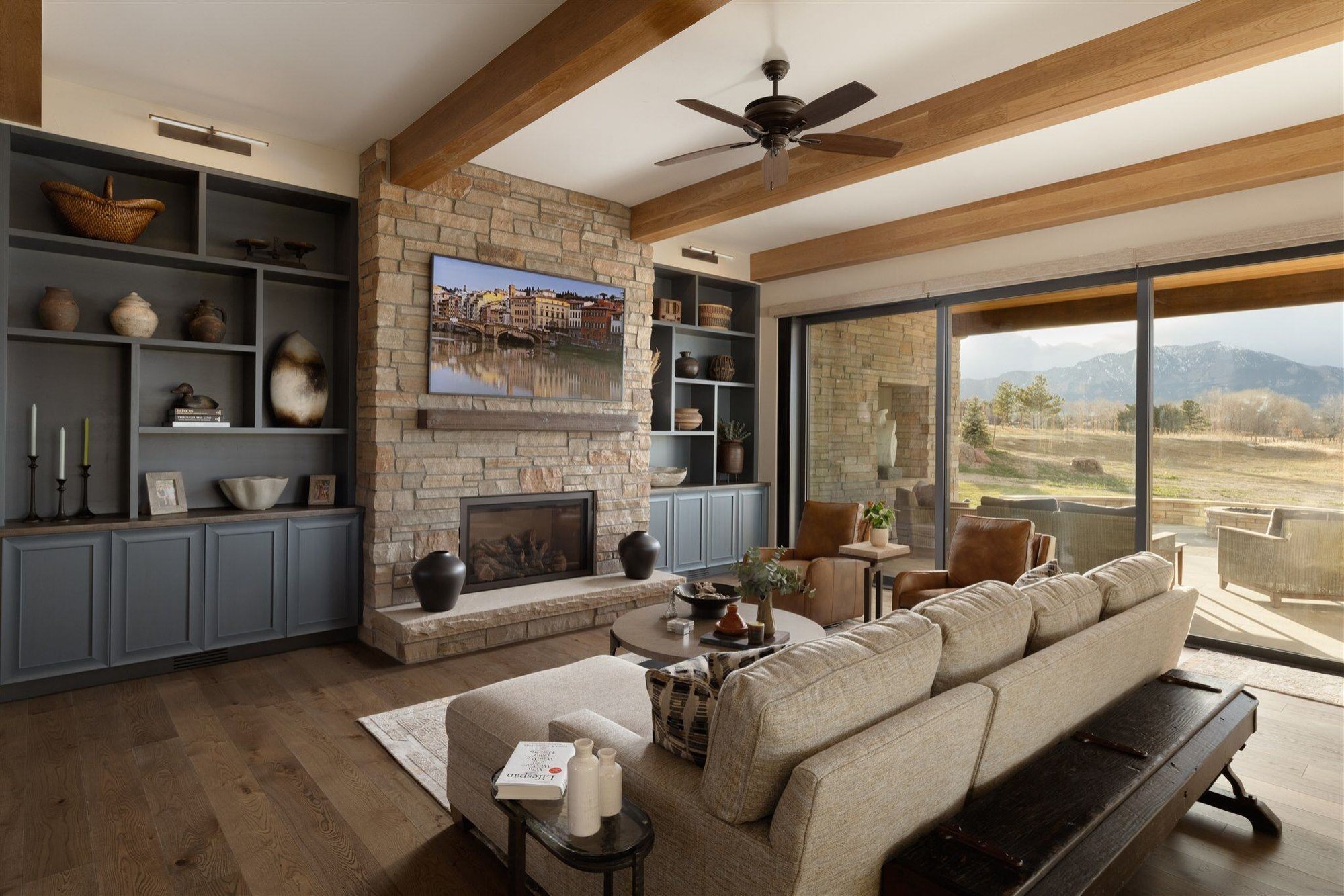 luxury living room with exposed wood beams, stone fireplace, and custom built in wall shelving storage