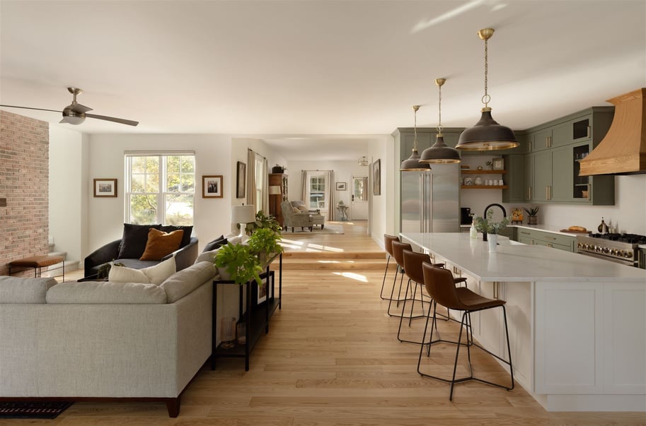 Open layout kitchen and living area with green kitchen cabinets, kitchen island seating, exposed brick wall, and custom lighting