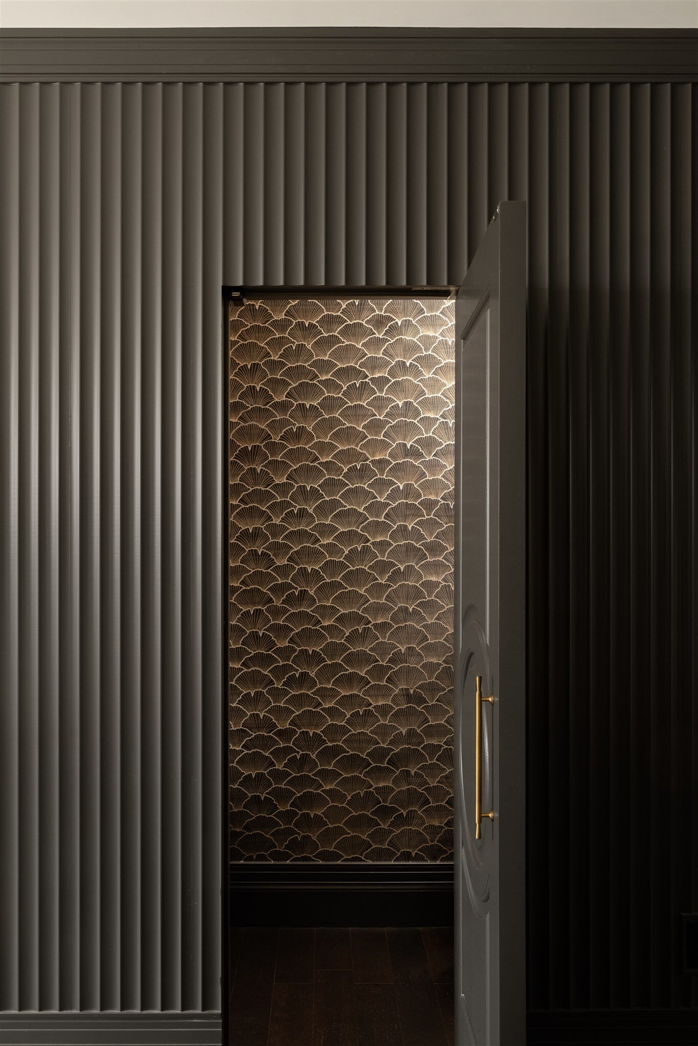 Textured dark wall with a door to a wallpapered bathroom