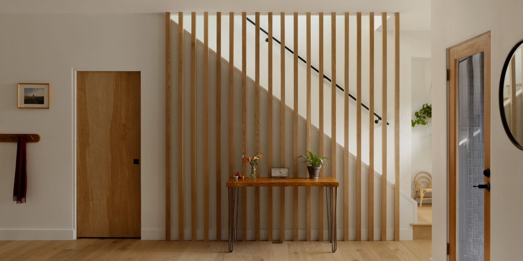 Remodeled entryway with light wood floors and doors and paneled staircase