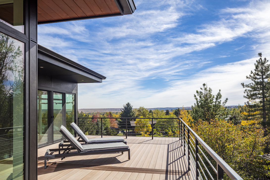 Petra Custom Builders' home featuring a spacious deck with comfortable lounging chairs, offering a serene view of a lush landscape under a vast blue sky with wispy clouds